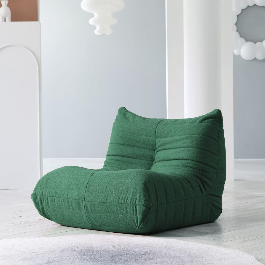 A distinctive green caterpillar-shaped floor armchair placed on a wooden floor in a room with light blue walls.
