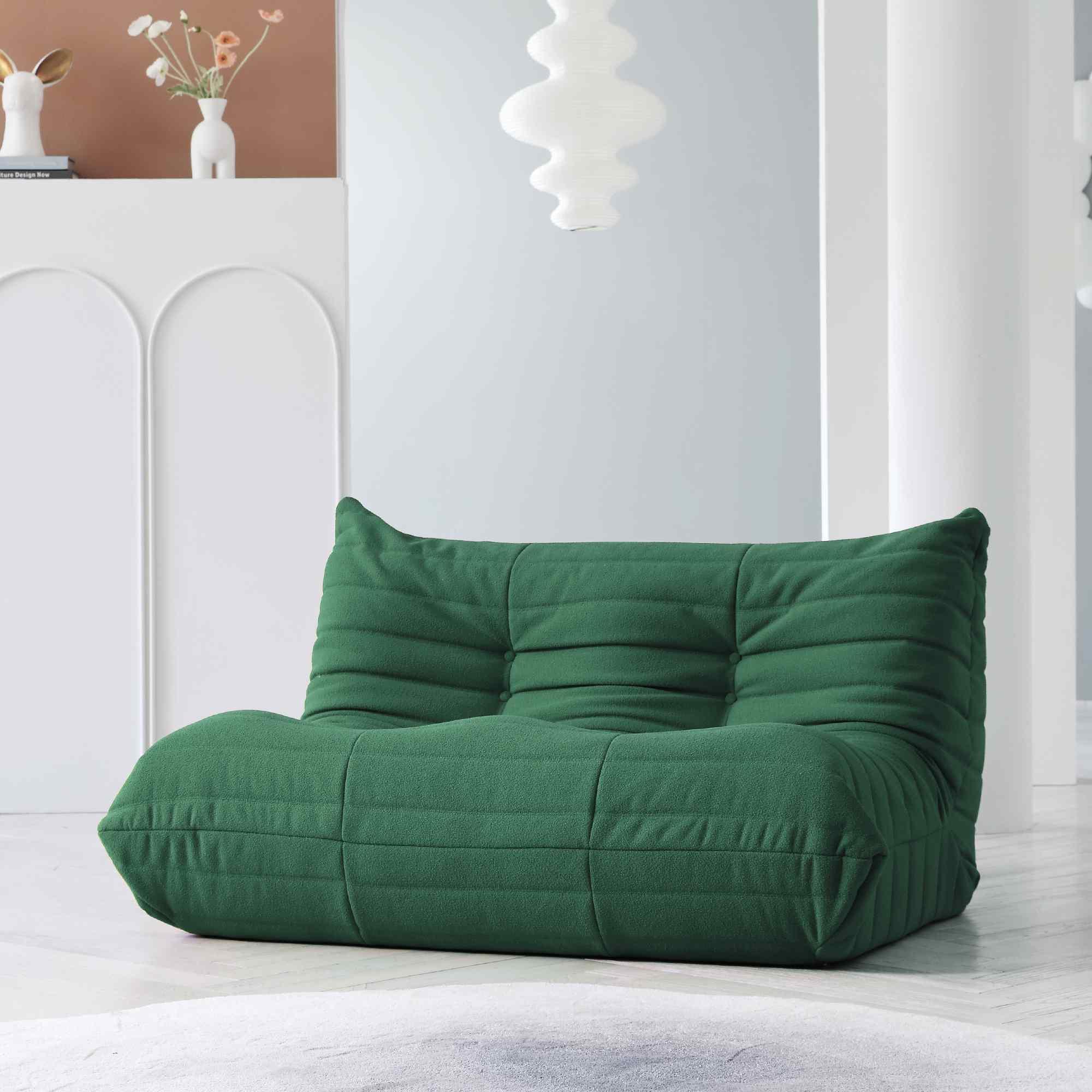 A green, caterpillar-shaped Togo sofa on a wooden floor with a light blue wall in the background.