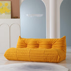 A distinctive yellow caterpillar-shaped 3-seater Togo sofa placed on a white floor in a room with light-colored walls and a painting in the background.