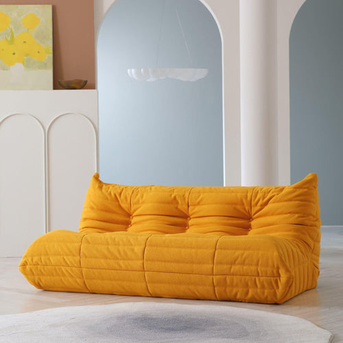 A distinctive yellow caterpillar-shaped 3-seater Togo sofa placed on a white floor in a room with light-colored walls and a painting in the background.