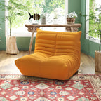 A distinctive yellow caterpillar-shaped floor sofa placed on a patterned rug in a room with green walls and a wooden table.
