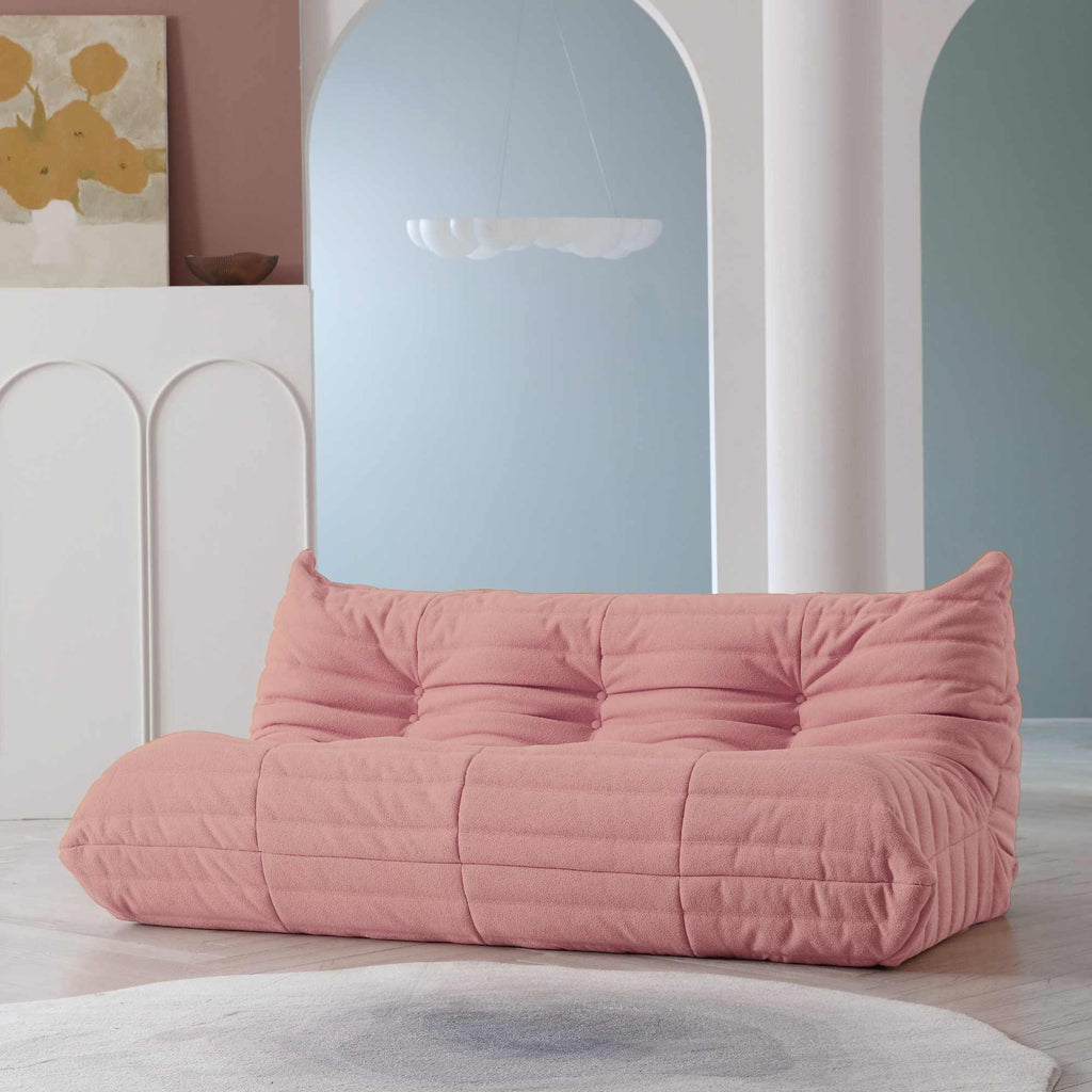 A distinctive pink caterpillar-shaped 3-seater Togo sofa placed on a white floor in a room with light-colored walls and a painting in the background.