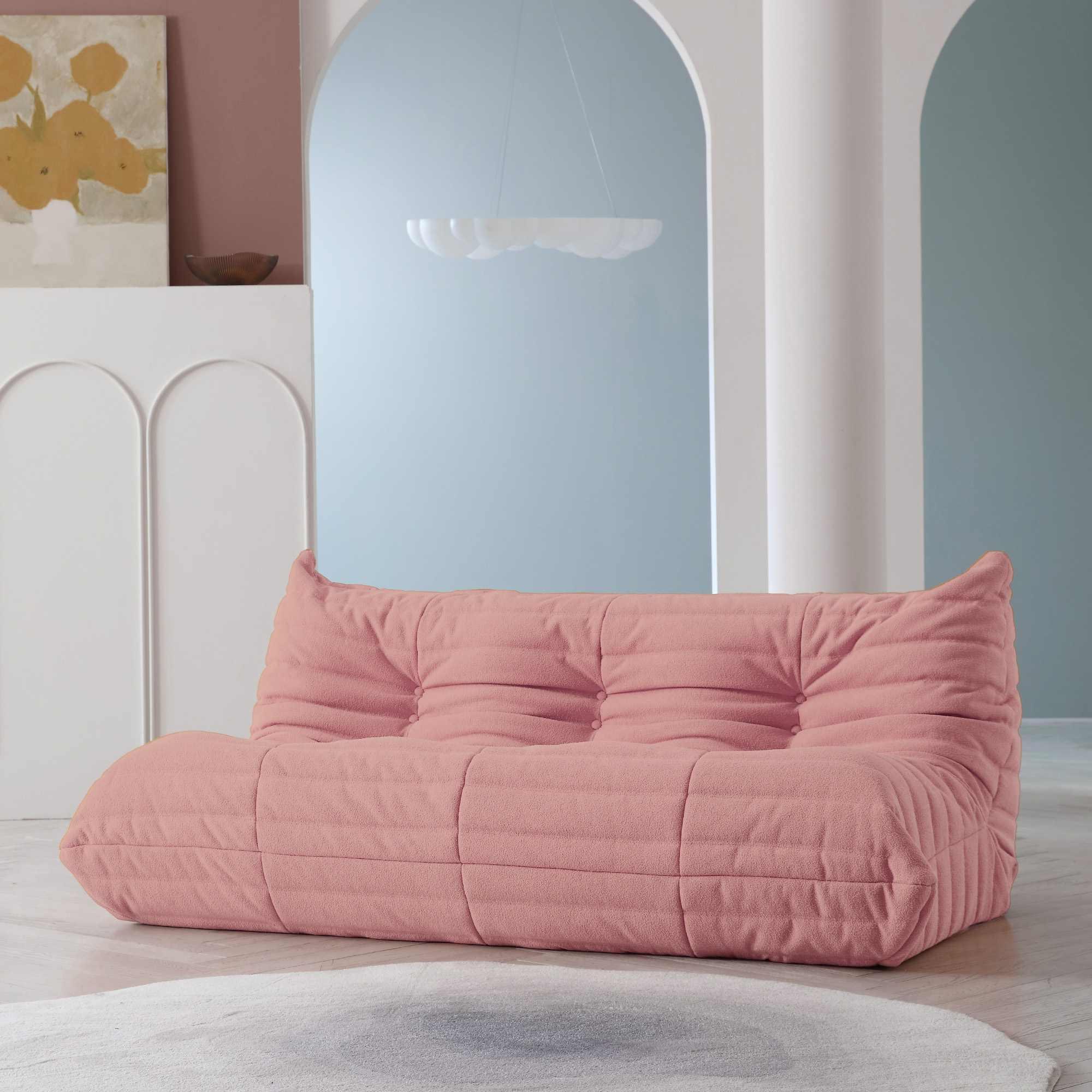 A distinctive pink caterpillar-shaped 3-seater Togo sofa placed on a white floor in a room with light-colored walls and a painting in the background.