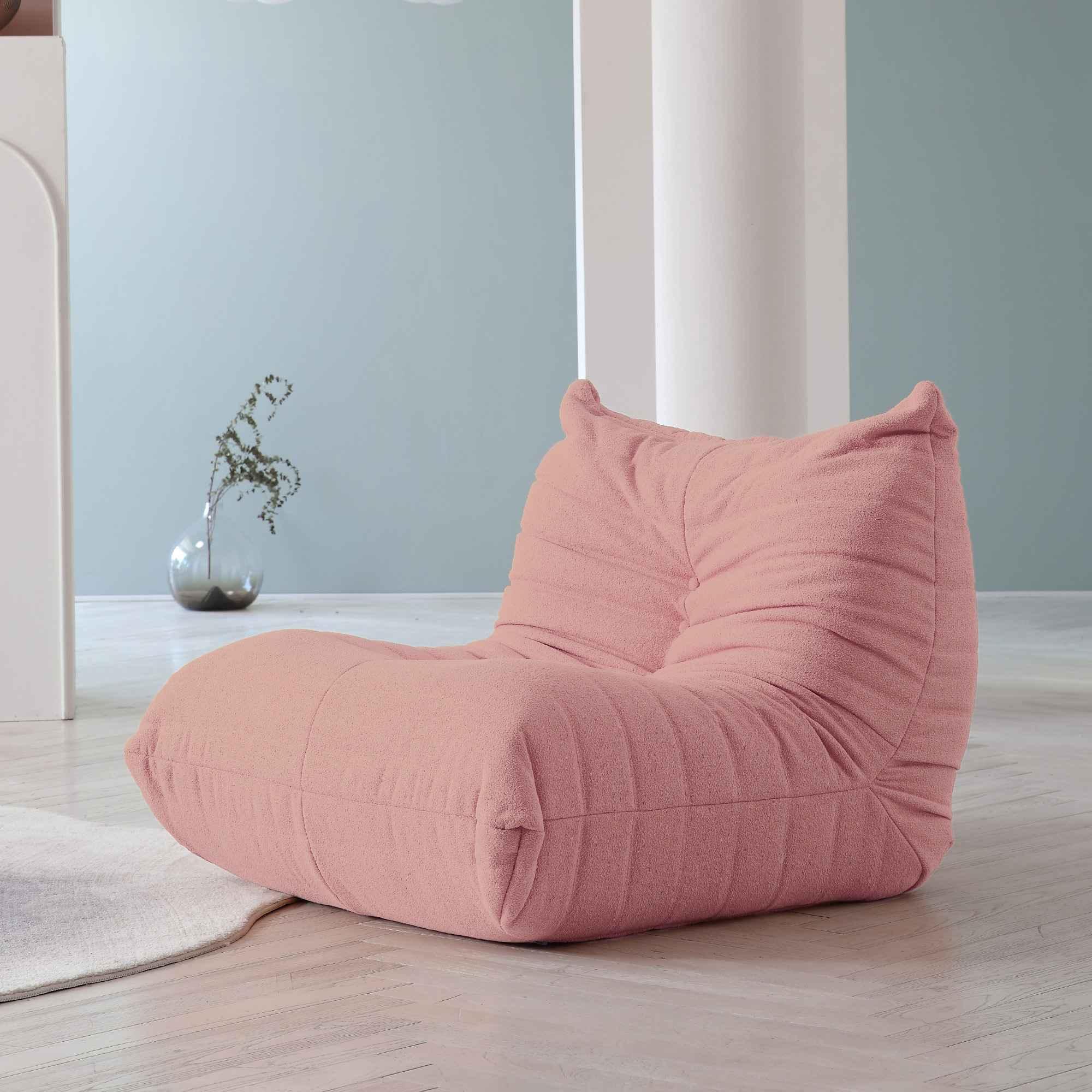 A pink caterpillar-shaped floor armchair placed on a wooden floor in a room with light blue walls.
