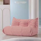 A pink, caterpillar-shaped Togo sofa on a wooden floor with a light blue wall in the background.