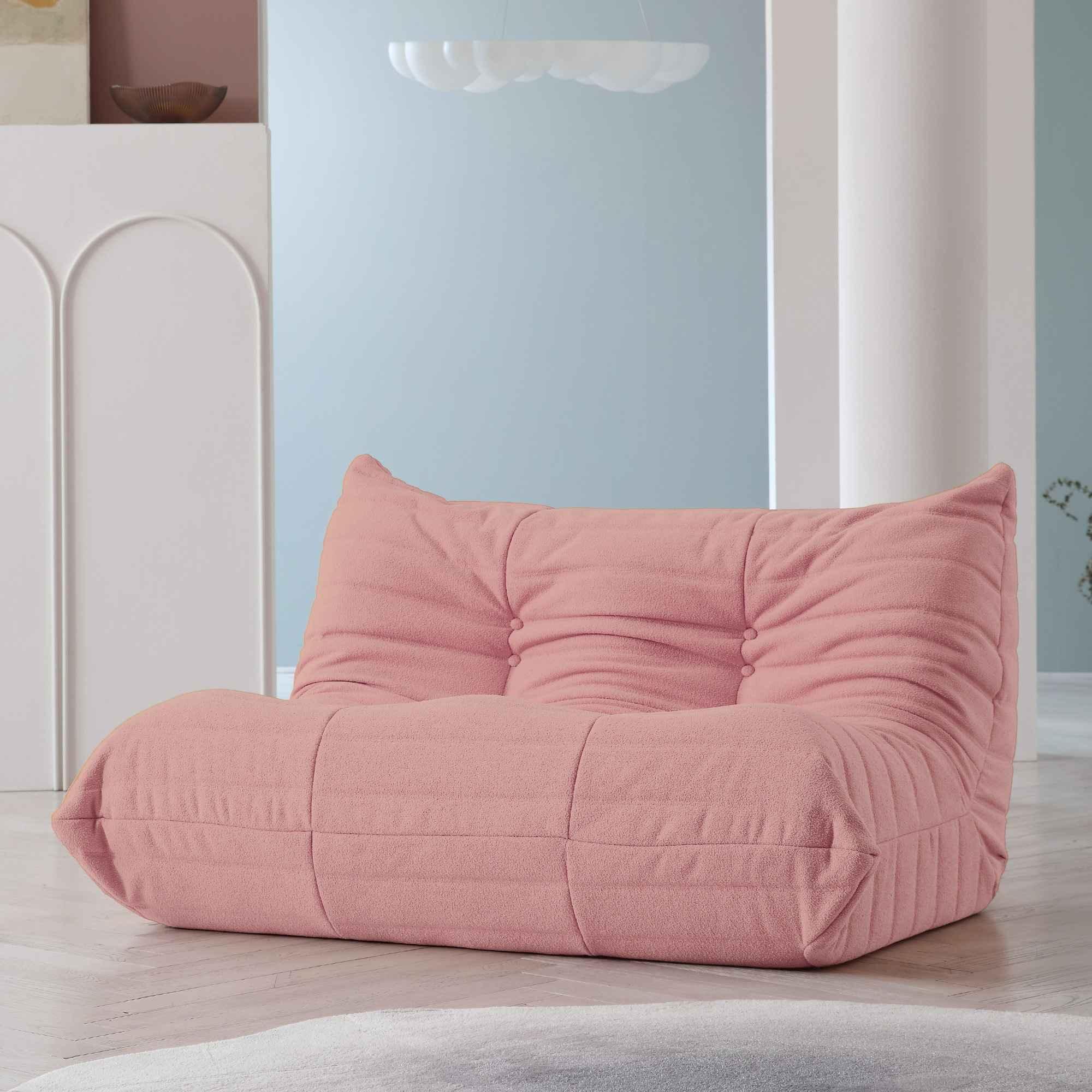 A pink, caterpillar-shaped Togo sofa on a wooden floor with a light blue wall in the background.