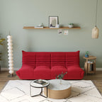 A red, caterpillar-shaped Togo sofa with a plush texture, situated in a room with minimalist decor, on a patterned rug.