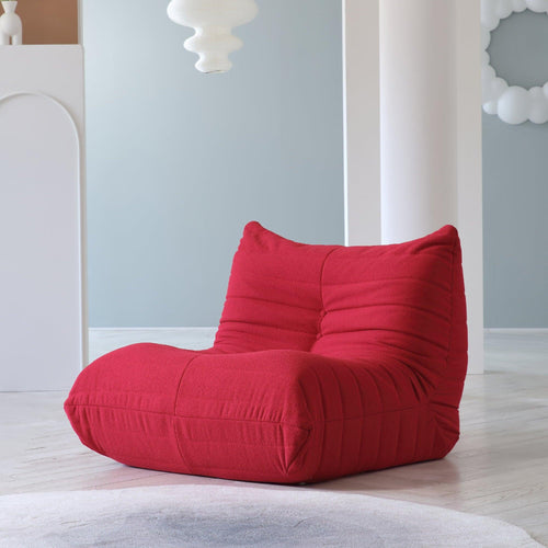 A red caterpillar-shaped floor armchair placed on a wooden floor in a room with light blue walls.