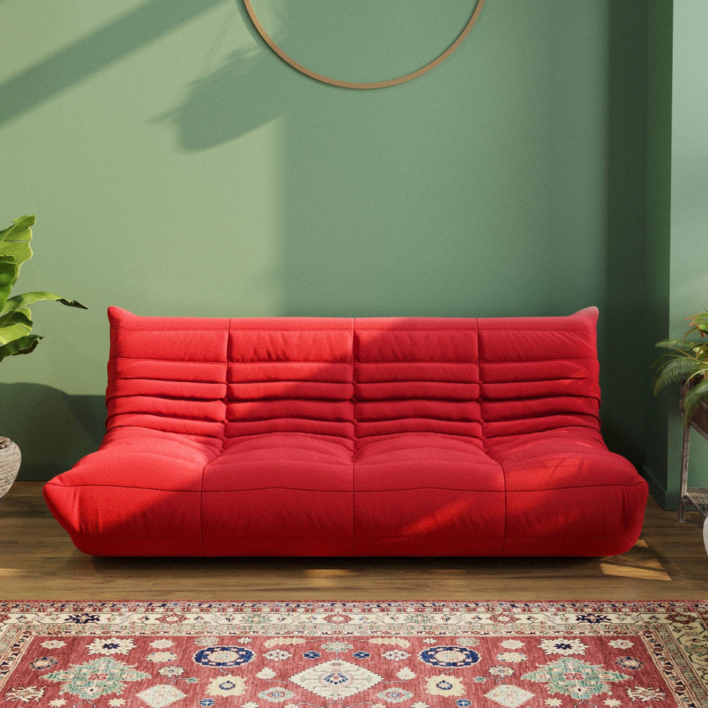 A red caterpillar-shaped 3-seater Togo sofa placed on a wooden in a room with green-colored walls.