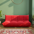 A red caterpillar-shaped 3-seater Togo sofa placed on a wooden in a room with green-colored walls.