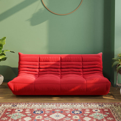 A red caterpillar-shaped 3-seater Togo sofa placed on a wooden in a room with green-colored walls.