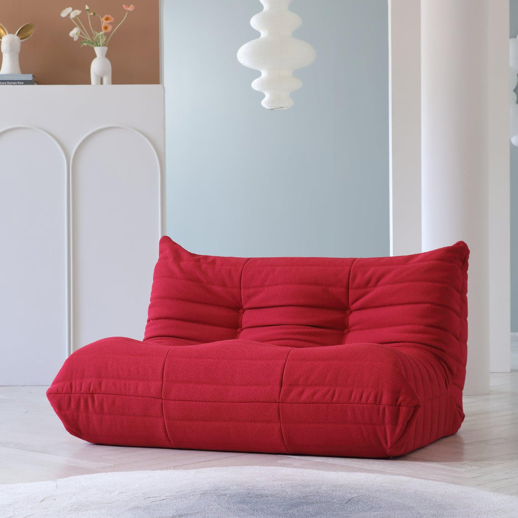 A red, caterpillar-shaped Togo sofa on a wooden floor with a light blue wall in the background.