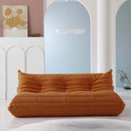 A distinctive brown caterpillar-shaped 3-seater Togo sofa placed on a white floor in a room with light-colored walls and a painting in the background.