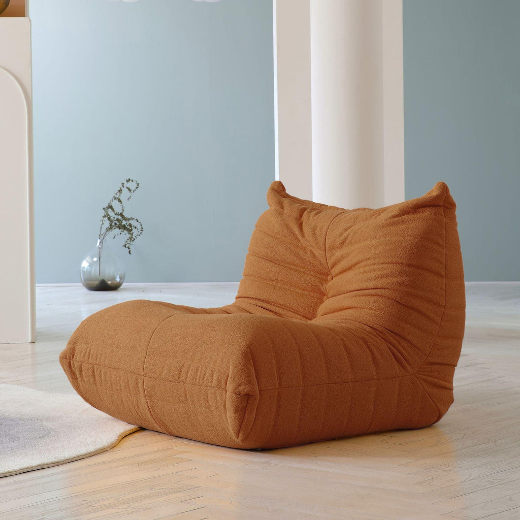 A brown caterpillar-shaped floor armchair placed on a wooden floor in a room with light blue walls.