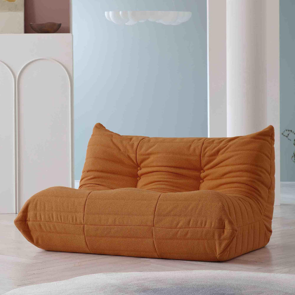 A brown, caterpillar-shaped Togo sofa on a wooden floor with a light blue wall in the background.
