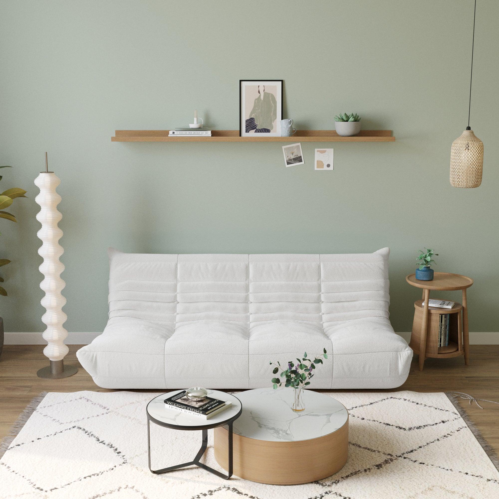 A white, caterpillar-shaped Togo sofa with a plush texture, situated in a room with minimalist decor, on a patterned rug.