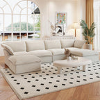 A beige U-shaped linen 6-seat sectional sofa with a storage ottoman situated in a bright room with large windows, alongside a low coffee table with items on it.