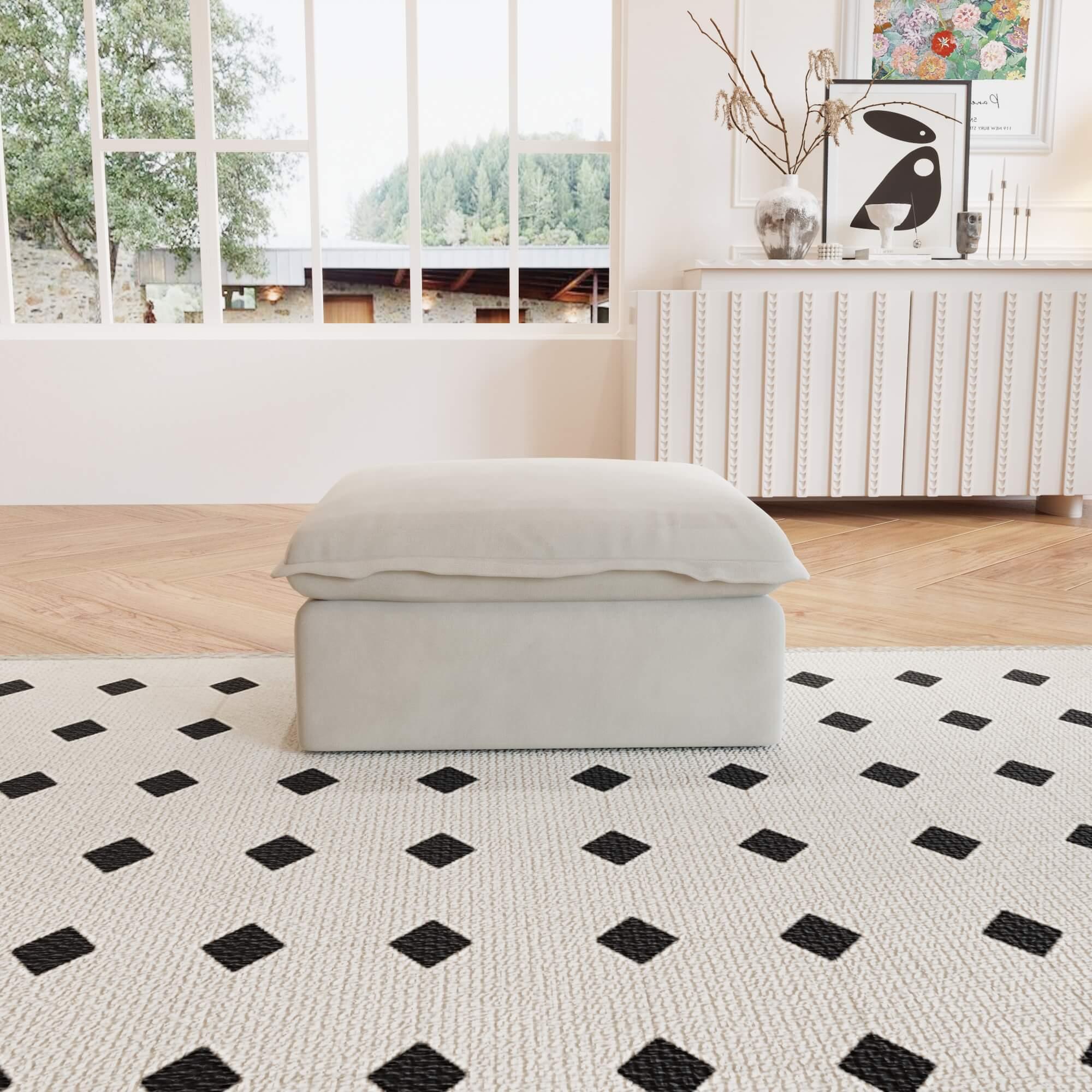A beige linen sectional ottoman with storage compartment placed on a black and white patterned rug in a living room setting.