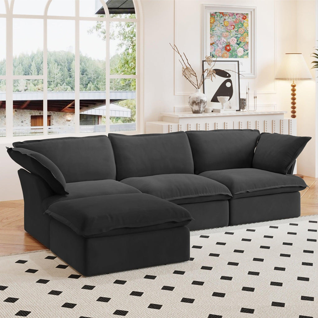 A black L-shaped linen sectional sofa with a storage ottoman positioned in a bright room with large windows, alongside a patterned rug and in front of a wall with artwork.