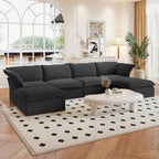 A black U-shaped linen sectional sofa with a storage ottoman situated in a bright room with large windows, alongside a low coffee table with items on it.