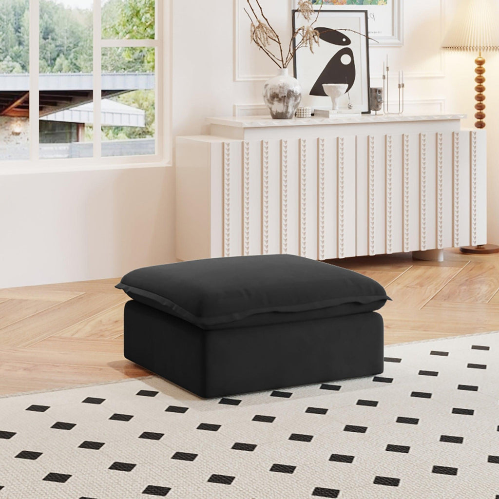 A black linen ottoman with a cushion on top, placed on a black and white patterned rug in a room with a window and a cozy interior decor.