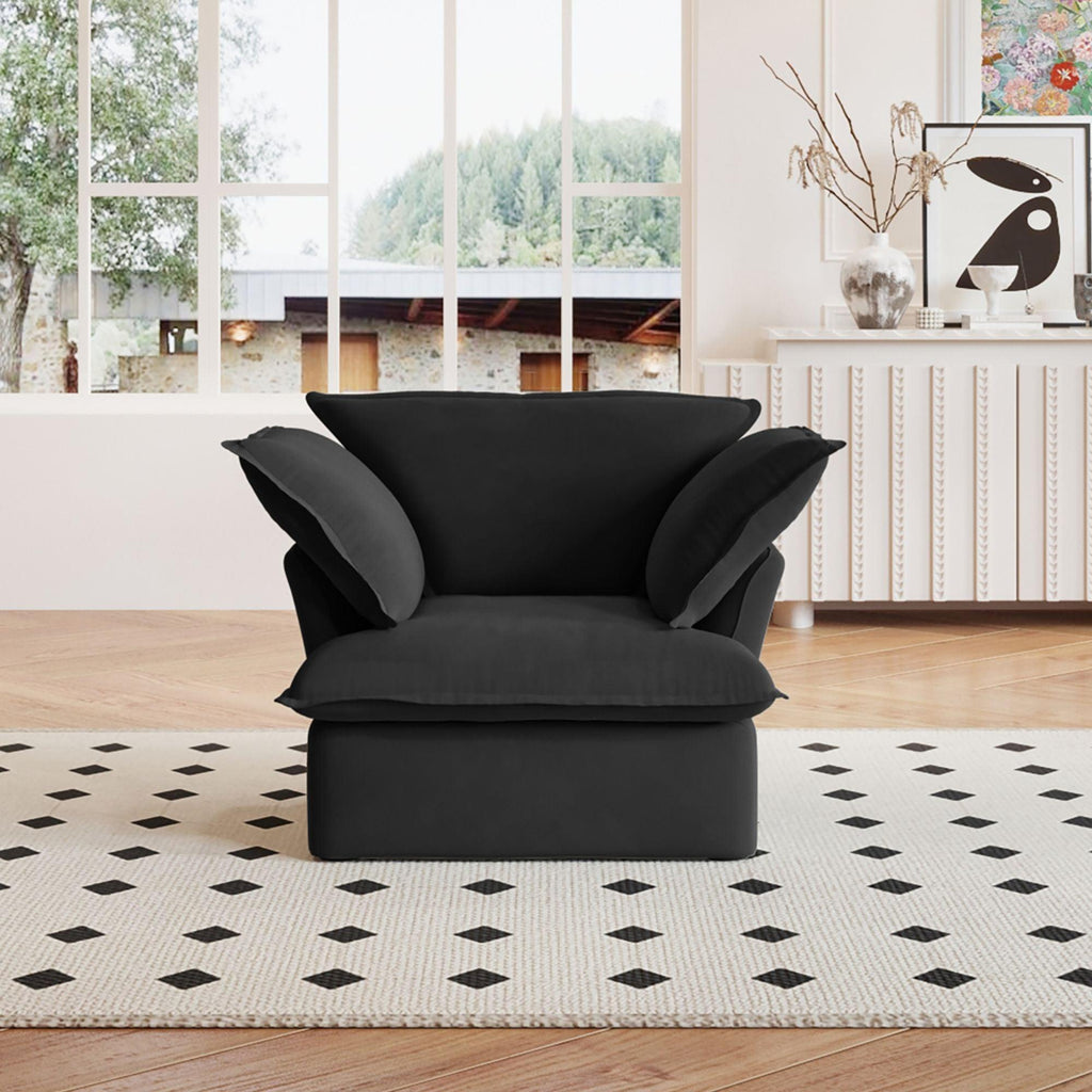 A black linen armchair with a solid frame and washable covers, placed on a patterned rug in a bright room.