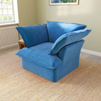 A blue velvet accent chair with a cushioned backrest and seat, placed in a room with a light green wall and a framed picture on the wall.