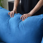 Person pressing on the back cushion of an blue sofa to show its softness