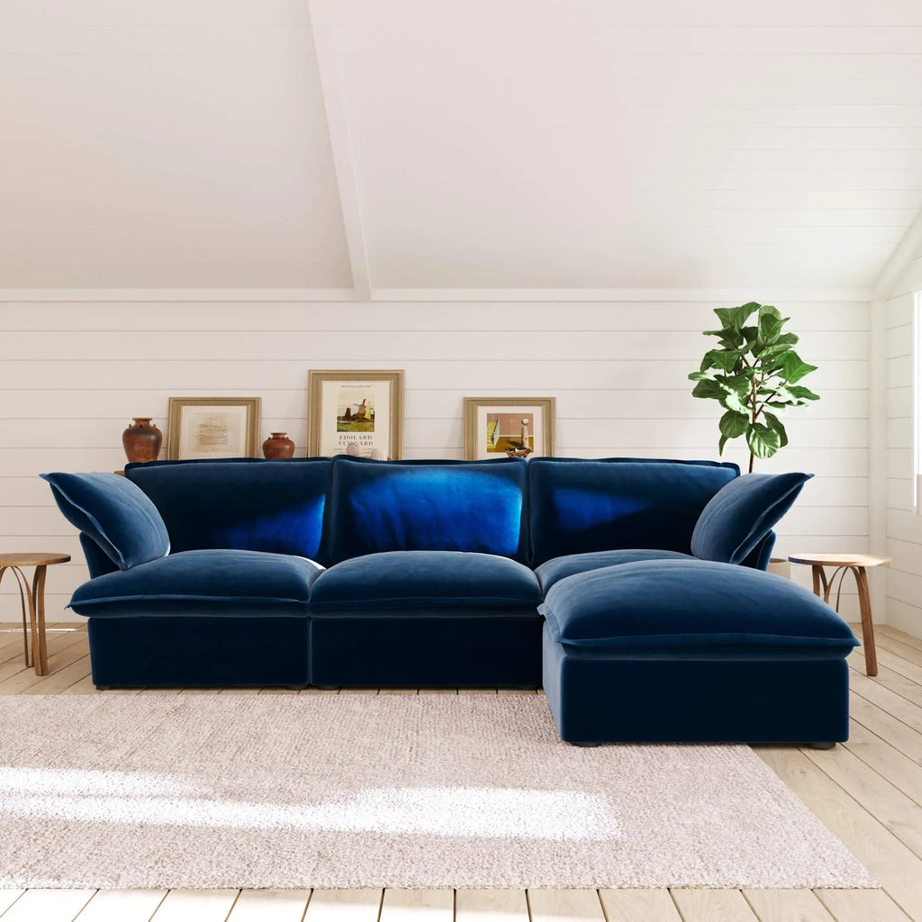 Dark blue L-shaped 4 -seater sectional sofa in a room with white walls, a plant, and framed pictures.