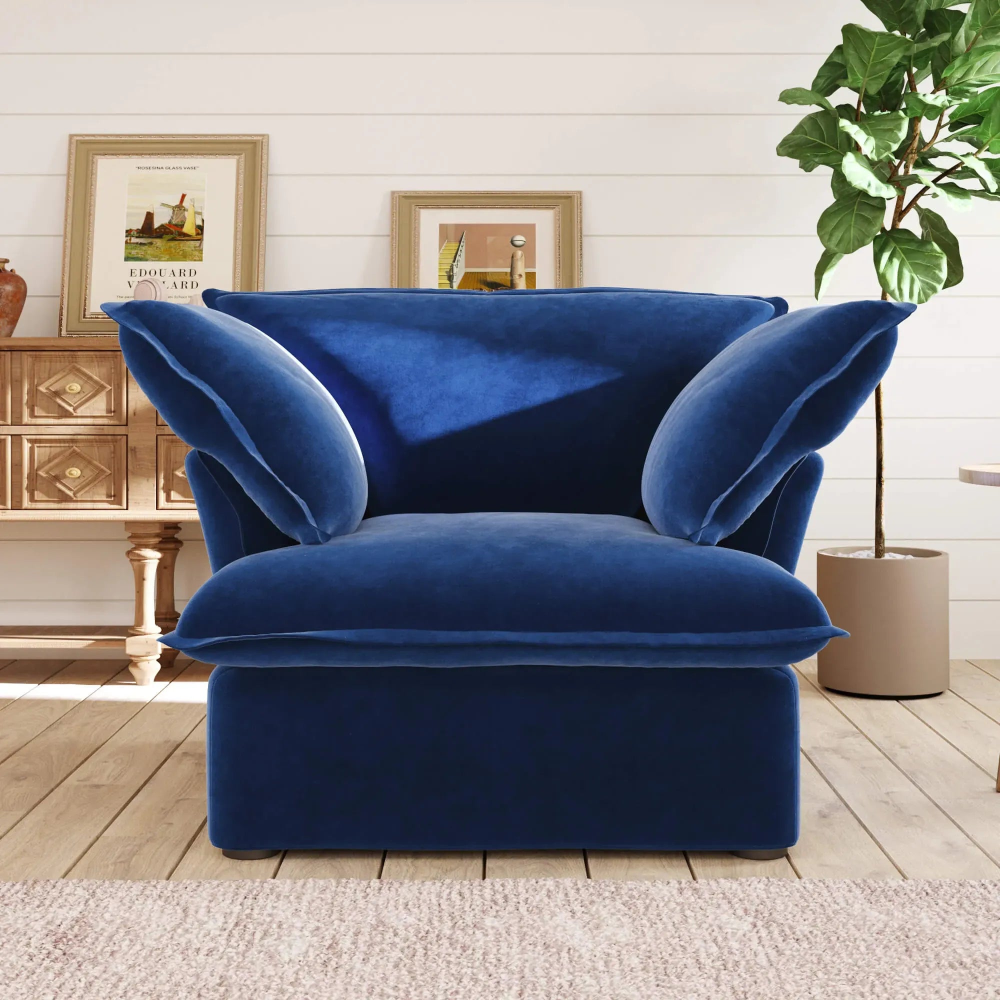 Dark blue armchair in a living room setting with a plant and framed pictures on the wall.