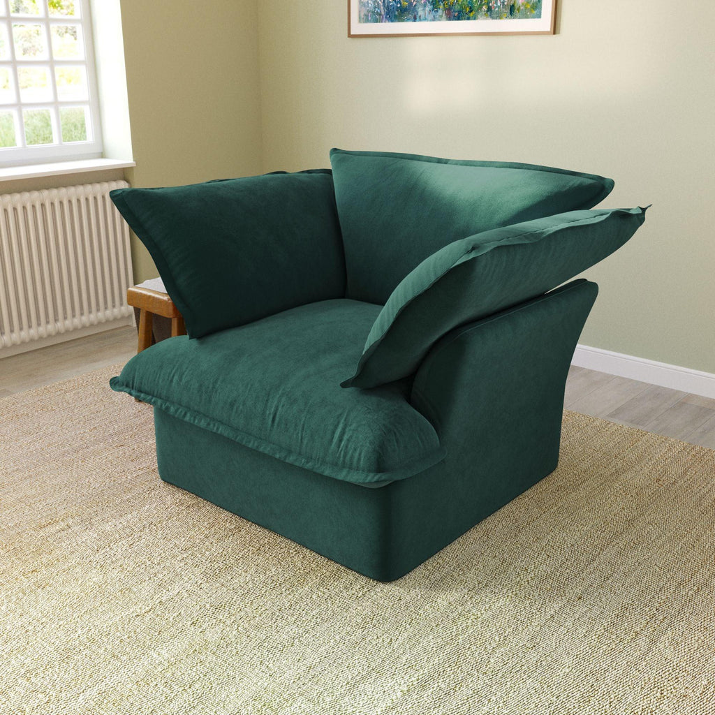 A green velvet accent chair with a cushioned backrest and seat, placed in a room with a light green wall and a framed picture on the wall.