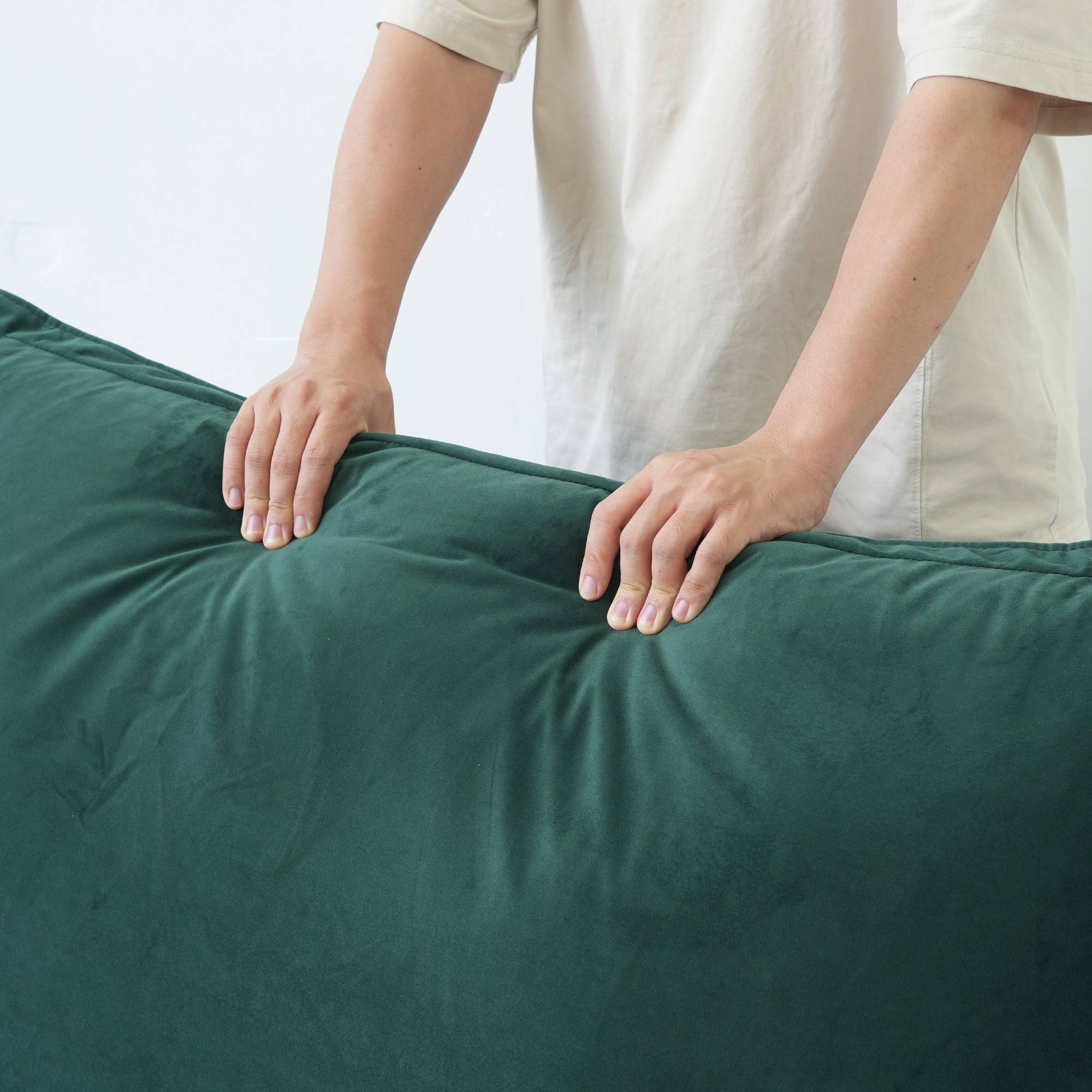 Person pressing on the back cushion of a green sofa to show its softness