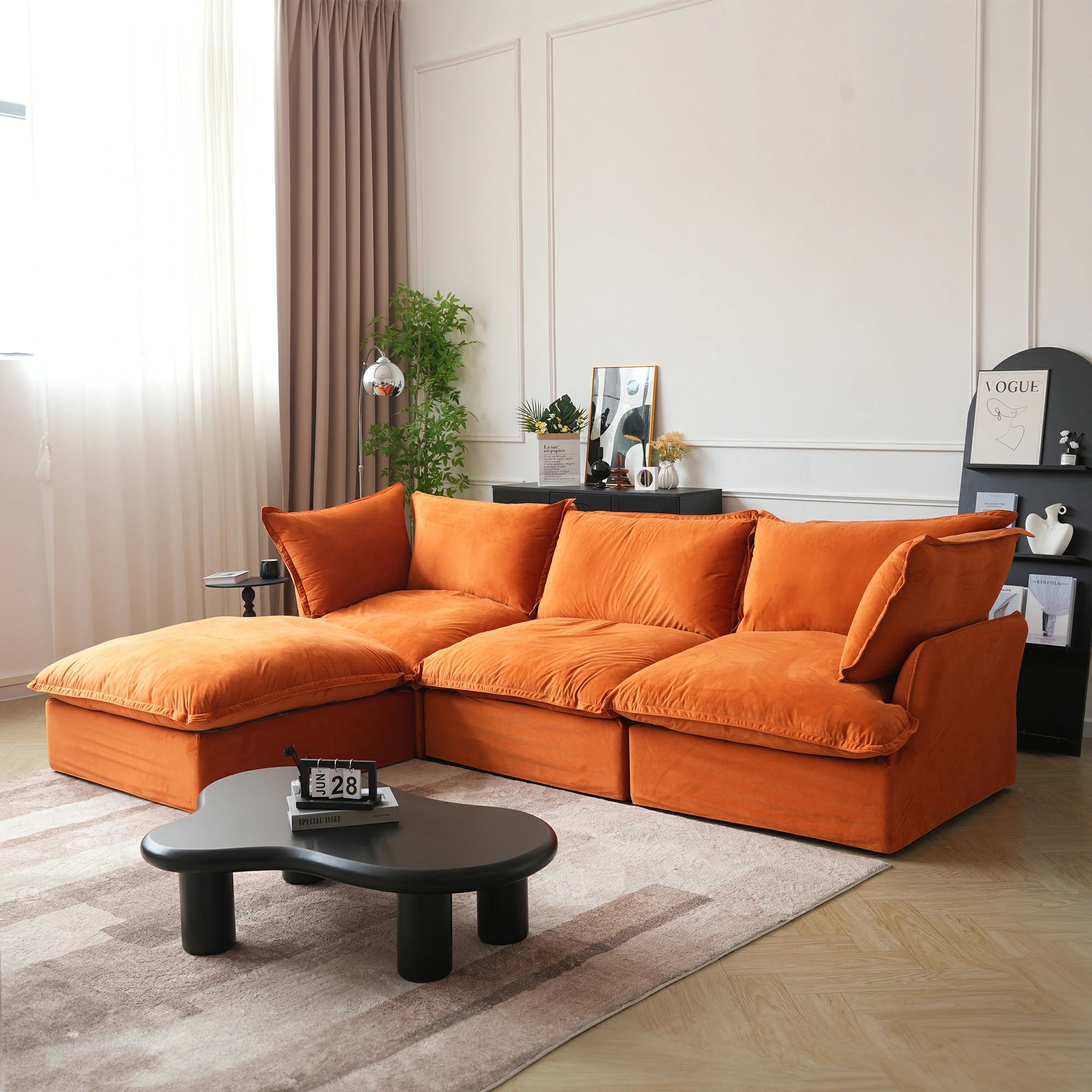 A modern orange velvet sectional sofa with a hidden storage ottoman, shown in a room with a round black coffee table in front.