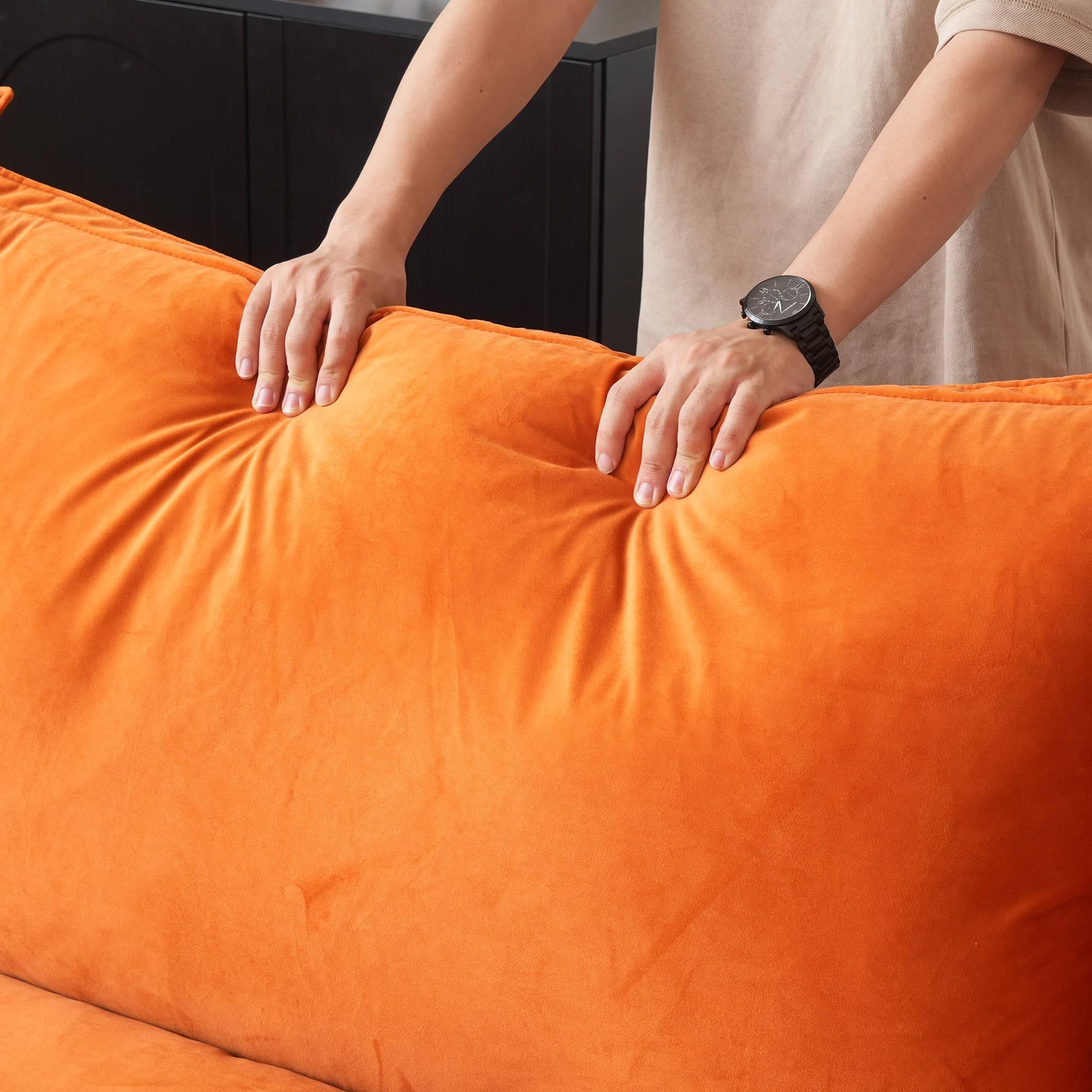 Person pressing on the back cushion of an orange sofa to show its softness