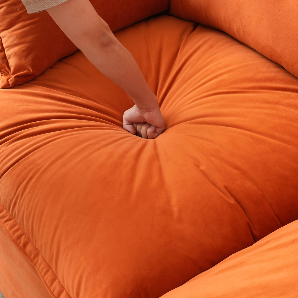 Person pressing on the seat cushion of an orange sofa to show its softness.