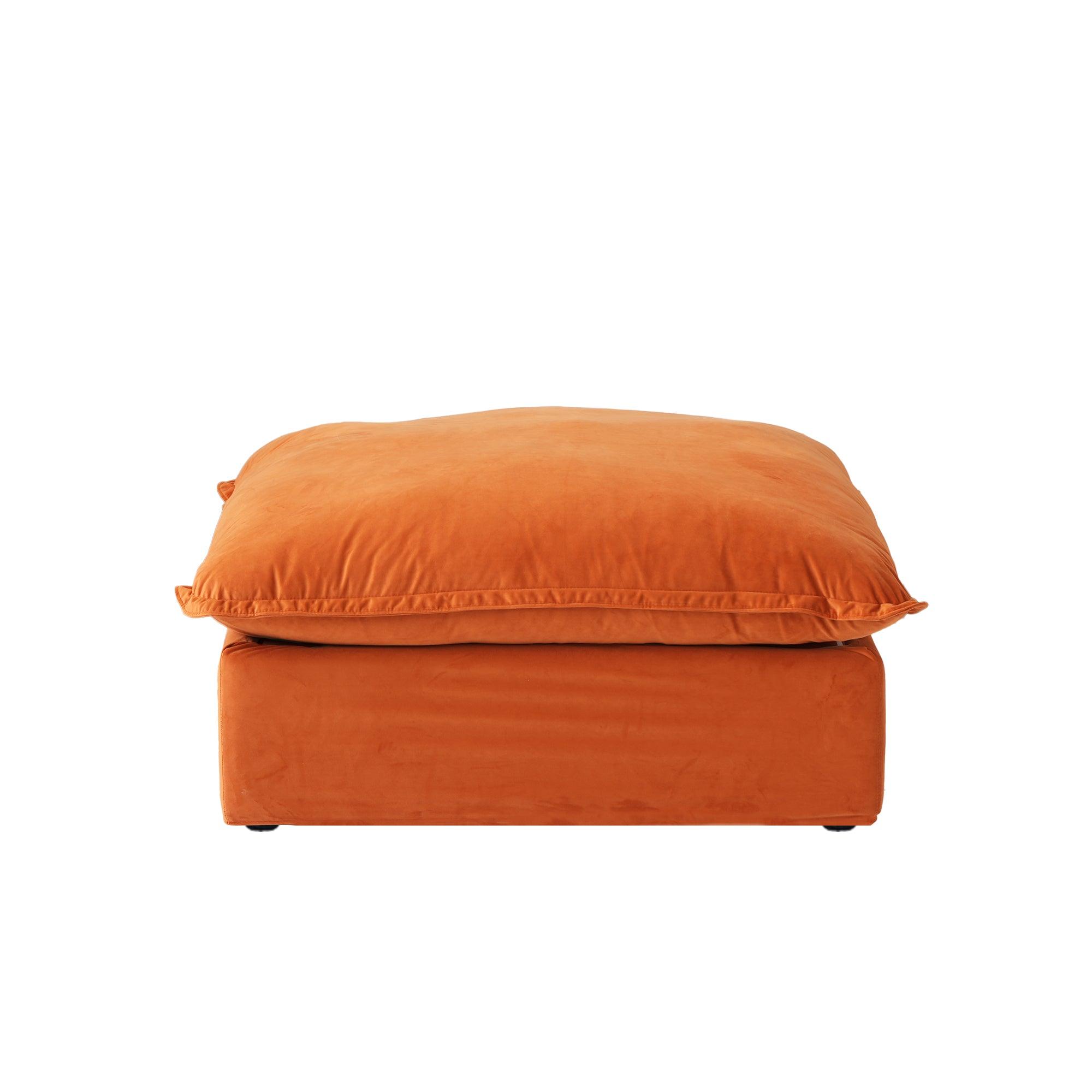 An orange velvet pouf ottoman with plush upholstery, shown with a removable cover.