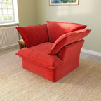 A red velvet accent chair with a cushioned backrest and seat, placed in a room with a light green wall and a framed picture on the wall.