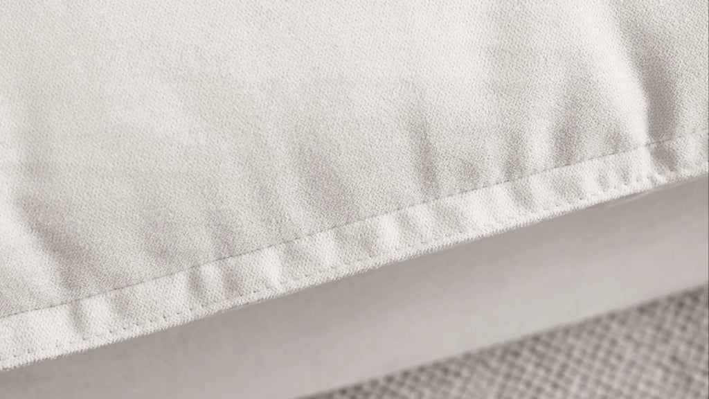 Close-up of a rim of a pillow of a white sectional sofa to show careful stitches