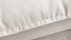 Close-up of a rim of a pillow of a white sectional sofa to show careful stitches