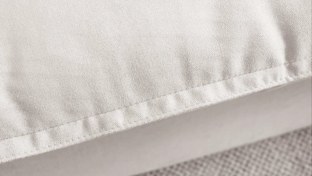 Close-up of a rim of a pillow of a white sectional sofa to show careful stitches
