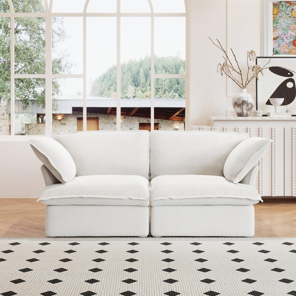 A white loveseat linen sectional sofa with modular design placed on a patterned rug in a bright living room setting.