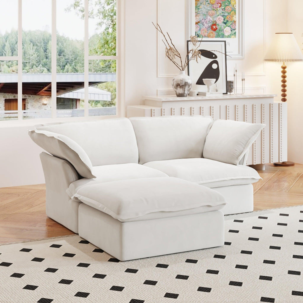 A white chaise lounge loveseat linen sectional sofa with a modular design and a storage ottoman, placed on a patterned rug in a bright living space.