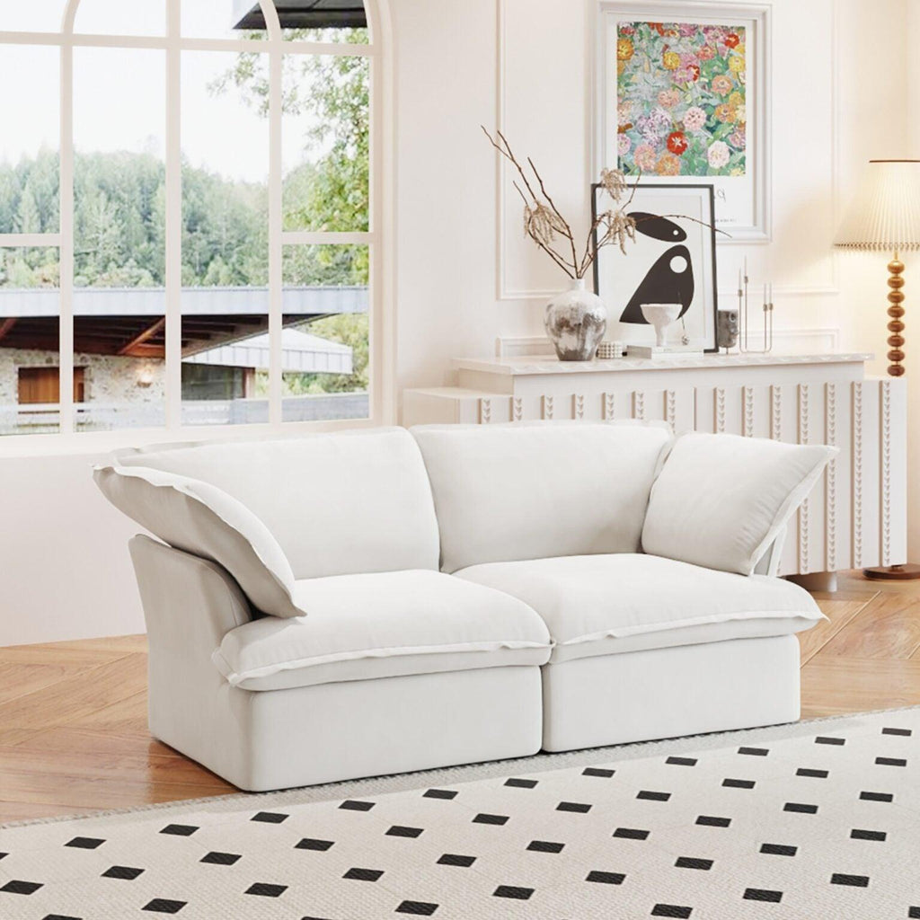 A white loveseat linen sectional sofa with modular design placed on a patterned rug in a bright living room setting.