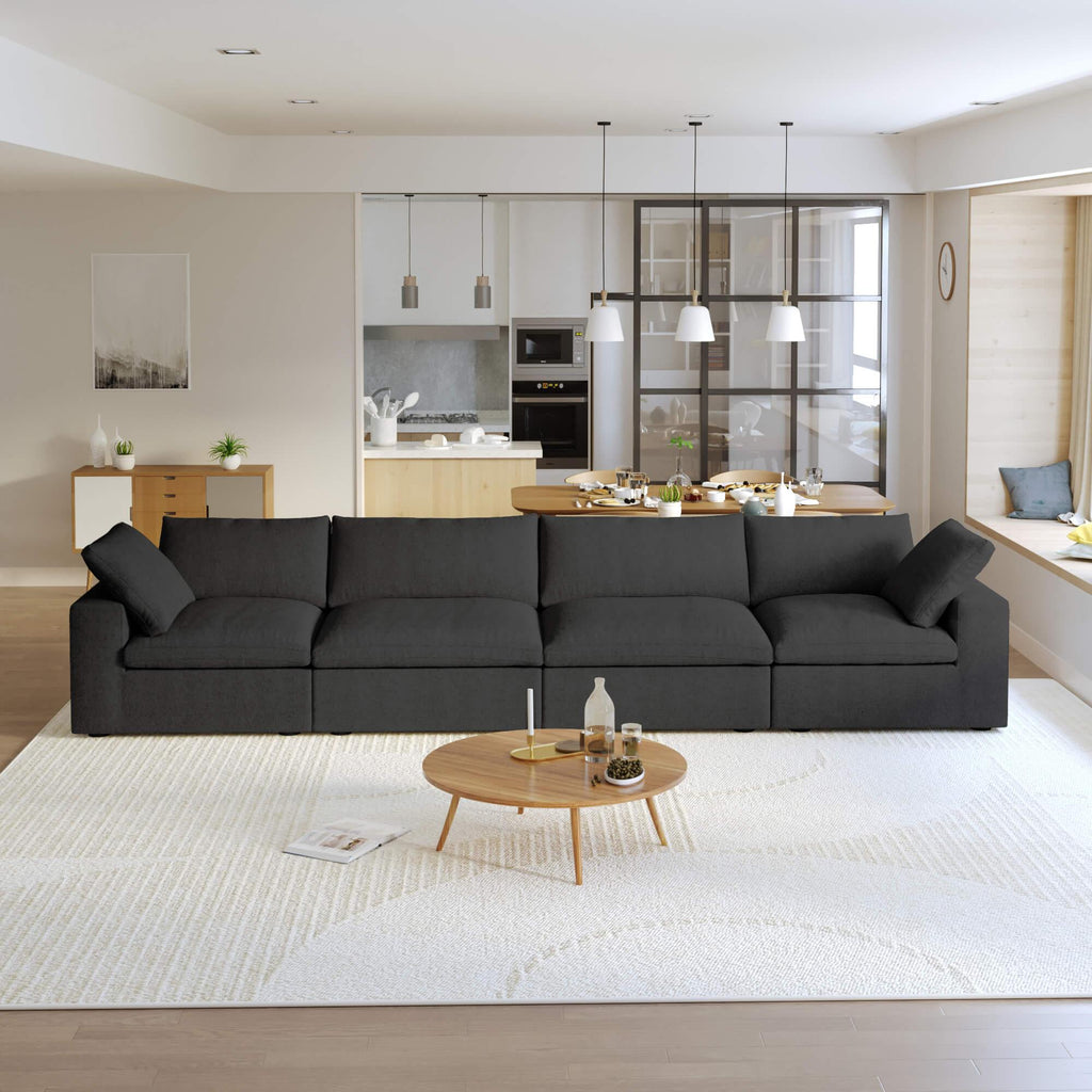 A modern black sectional sofa in a living room setting, featuring a 4-seater configuration with a modular design, down-filled cushions, and a clean, white color scheme.