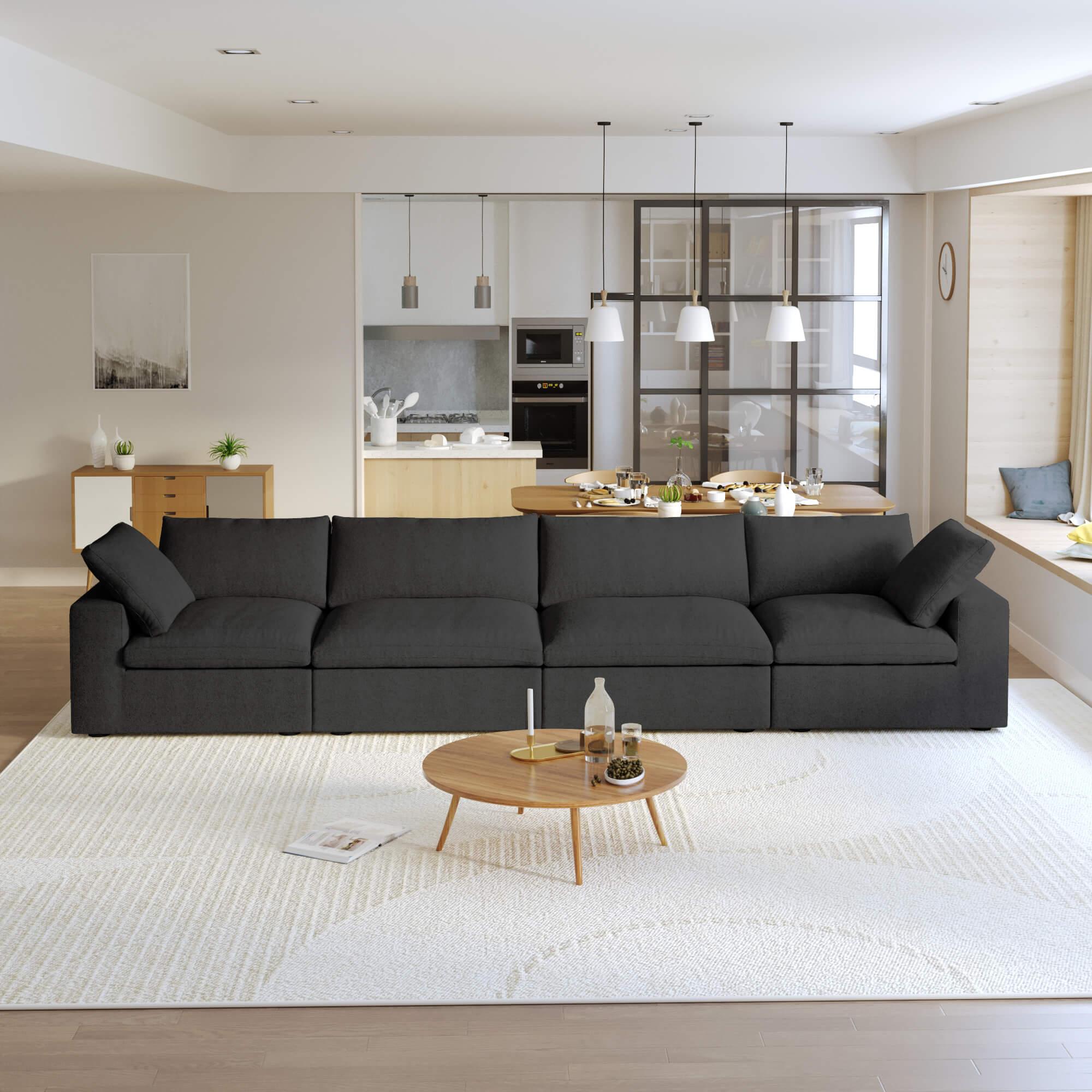 A modern black sectional sofa in a living room setting, featuring a 4-seater configuration with a modular design, down-filled cushions, and a clean, white color scheme.