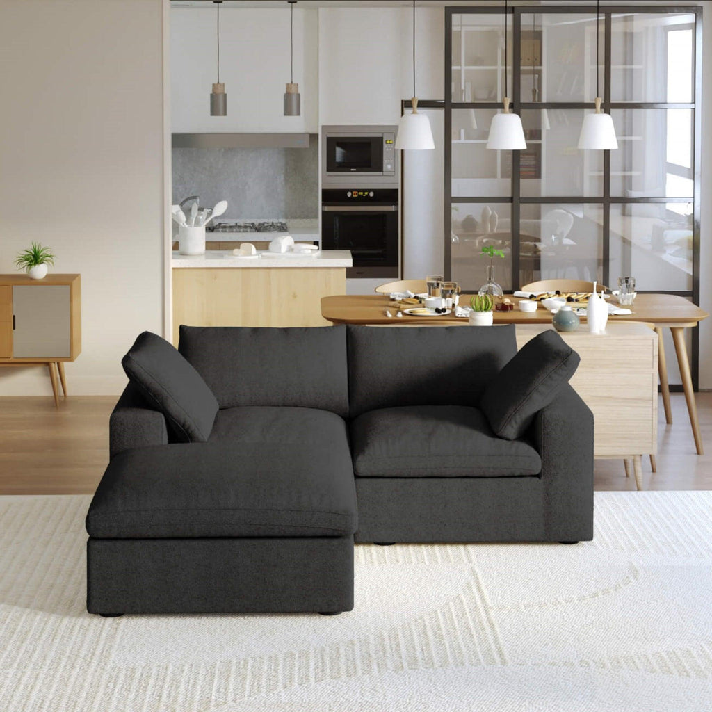 A black modular sectional sofa with a storage ottoman in a modern living room setting.