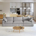 A modern gray 3-seater sectional sofa in a living room setting with a round wooden coffee table in front and a kitchen area in the background.