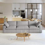A modern gray 3-seater sectional sofa in a living room setting with a round wooden coffee table in front and a kitchen area in the background.