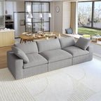 A modern gray 3-seater sectional sofa in a living room setting with a round wooden coffee table in front and a kitchen area in the background.