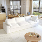 A modern white 3-seater sectional sofa in a living room setting with a round wooden coffee table in front and a kitchen area in the background.